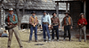Six men in cowboy attire stand outside rustic wooden buildings, each wearing hats and holding guns, appearing to prepare for a confrontation in an Old West setting reminiscent of a scene from a Zane Grey movie—a perfect addition to any classic western DVD collection. Rewritten using product data: Six men in cowboy attire stand outside rustic wooden buildings, each wearing hats and holding guns, readying themselves for a standoff straight out of the Old West—a scene captured in “Robber’s Roost (1955) DVD,”