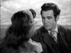 A man in a suit gazes at a woman with wavy hair as they share a serious conversation outdoors, captured in a black-and-white scene evocative of classic films like Trail Street (1947) on DVD.