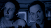 Two people sit closely together in a dimly lit space, looking ahead with wide eyes and tense expressions, as if startled by something just out of view—perfectly capturing the suspenseful energy found in Australian horror-comedy gems like the “Undead (2003) DVD.”.