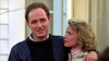 A man with short brown hair in a dark sweater stands outdoors, his arm around a blonde woman in a light jacket who looks up at him. They hold a rare classic: The Stepfather (1987) DVD, in front of a light-colored building.