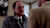 A man with glasses, a mustache, and a patterned overcoat stands indoors facing another person’s back, evoking the suspense of The Stepfather (1987) DVD. A clock at 4:00 and curtained windows add to the psychological thriller atmosphere.