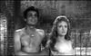 A shirtless man stands beside a woman with long hair in front of a brick wall, both gazing off-screen in a black-and-white scene from “The Woman Eater (1958)” DVD—a cult classic movie highly sought after by collectors of rare and hard-to-find films.