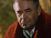 An older man with graying hair and a red knitted shawl looks sad, tears streaking his cheeks as he gazes downward, capturing an emotional moment reminiscent of scenes from the “Virus (1999) DVD.”.