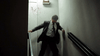 A man in a suit stumbles down a dimly lit stairwell, blood splatters visible on the wall behind him—an unforgettable scene that could be straight out of Stalking Laura (1993) on DVD, with its intense and suspenseful depiction of workplace stalking.