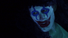 A person with long hair, their face painted white with bold blue and red clown makeup, is depicted in moody, low lighting that evokes the dark and unsettling atmosphere found in cult splatter films like Clownado (2019), now available on DVD.