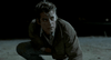 A young man with wet hair and a serious expression kneels on the ground at night, dressed in a brown jacket and jeans, gazing upward under dim lighting—capturing the moody atmosphere featured in *Near Dark (1987)* DVD.