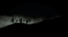 A group of people stands silhouetted on a hilltop shrouded in mist and darkness, illuminated by backlighting that evokes the eerie, dramatic atmosphere of the 1980s horror film “Near Dark (1987),” now available on DVD.