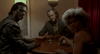 Three people sit around a round table scattered with bullets in a dimly lit room; one smokes a cigarette, another is clad in a suit, and the third—with disheveled gray hair—casts a glance back toward the camera, evoking the gritty atmosphere of an intense 1980s horror film like *Near Dark (1987)* on DVD from acclaimed director Kathryn Bigelow.