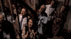 Seven adults in vintage clothing peer up through staircase railings with concerned or curious expressions inside a dimly lit house, capturing the tense atmosphere reminiscent of *The Tenant (1976) DVD*, a classic psychological horror film inspired by directors like Roman Polanski.