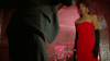A woman in a red strapless dress and black gloves stands under an archway, gazing at a suited companion—evoking the unforgettable style and dark humor of cult classics like Vampire’s Kiss (1989), now on DVD. The dimly lit, pink-hued brick backdrop adds to the movie’s iconic atmosphere, perfect for fans seeking rare cinematic moments.