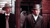 Two men in old-fashioned Western attire stand before a wooden building, looking serious—like a scene from The Last Gun (1964) DVD.