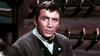 A man in 19th-century attire sits indoors with pistols on the wall—a scene from The Last Gun (1964) DVD, a must-have for classic western fans and collectors of rare movie DVDs.