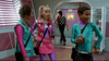 Three kids in colorful, futuristic outfits stand together indoors, holding drinks and chatting, while another person walks away through pink double doors in a brightly colored room—a scene reminiscent of 90s nostalgia movies like Zenon Girl of the 21st Century (1999) DVD or other rare Disney Channel original movie DVDs.