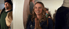 A woman with long blonde hair smiles and clasps her hands in excitement, standing indoors with people in the background, perhaps celebrating the discovery of “A California Christmas: City Lights (2021)” on DVD.