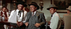 Three men dressed in old-style Western outfits stand at a saloon bar—one’s arm is in a sling, another wears a sharp gray suit. Scene from "Ride A Crooked Trail (1958) DVD.