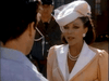 A woman in a peach suit and netted white hat speaks to a man outdoors, with a uniformed officer behind them—a scene from the classic TV miniseries "Monte Carlo" (1986), now available on rare movies DVD.