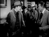 A group of men in Western attire stand indoors, conversing—one in a cowboy hat and vest, another with a light hat. This black-and-white scene evokes classic comedy as seen in "The Slowest Gun in the West (1960) DVD.