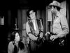 Three people stand in a black-and-white scene: a seated woman, a man in glasses and vest, and a cowboy with hat and holster—fans of classic comedy will enjoy this moment from The Slowest Gun in the West (1960) DVD.