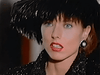A woman with blue eyes and red lipstick, adorned in a large black feathered hat, pearl earrings, and a sequined black outfit, looks surprised—capturing the glamour and intrigue found in classic films like *The Counterfeit Contessa (1994)* on DVD.