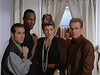 Four adults stand close together indoors, looking toward the camera with surprised or serious expressions—perhaps having just discovered a rare DVD of "The Counterfeit Contessa (1994)." Light-colored curtains and a lit lamp accent the background, adding to the cozy atmosphere reminiscent of enjoying classic movies on DVD.