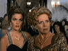 Two elegantly dressed women stand close together at a formal event, both looking surprised or concerned. The background shows other guests and chandeliers in a grand hallway—the kind of unforgettable scene featured in "The Counterfeit Contessa (1994)" DVD.