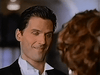 A man in formal attire smiles warmly at a person with curly reddish-brown hair, in a scene reminiscent of classic movies—perfectly capturing the charm and romance found in "The Counterfeit Contessa (1994)" on DVD. The softly blurred background draws focus to their interaction, evoking the timeless appeal of this beloved film.