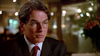A man wearing glasses, a dark suit, and a red tie sits indoors in soft lighting, gazing slightly to his left with a neutral expression—evoking the mysterious atmosphere of “Never Let Her Go (2001)” as seen on DVD.
