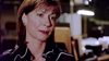 A woman with short brown hair and earrings stands thoughtfully in what appears to be an office or workspace, seemingly absorbed in contemplating the gripping details of “Never Let Her Go (2001) DVD,” a true crime miniseries.
