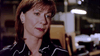 A woman with short brown hair, wearing a black blouse with white trim, looks thoughtful in a dimly lit office setting—her expression reminiscent of someone engrossed in the "And Never Let Her Go (2001) DVD.