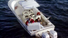 Two people on a white motorboat examine a large map or chart, evoking scenes from the true crime miniseries “Never Let Her Go (2001)” DVD. The boat, floating on deep blue water, is outfitted with twin outboard engines and equipped with navigational instruments and a lifebuoy.