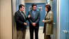 Three people in business attire stand talking in a narrow hallway with blue doors, looking serious and deeply engaged in discussion—as if delving into the twists of the true crime story portrayed in Never Let Her Go (2001) on DVD.