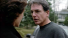 A man with gray hair and glasses wearing a dark sweater talks closely to another person outdoors, with trees and a house in the background—evoking the suspenseful atmosphere of “Never Let Her Go (2001)” DVD.