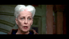 An older woman with white hair arranged in two rolls stands before a wooden door, wearing an expression of surprise or concern—reminiscent of a character you might see in “The Frighteners (1996)” on DVD.