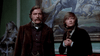 A man with a mustache and a younger man stand in front of a large gothic horror painting from the Dracula (1974) DVD in a room with a cobweb-covered statue.