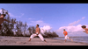 Four men are practicing martial arts on a sandy beach with trees and a cloudy sky in the background. Three wear white pants, while one stands out in an orange shirt and shorts. This lively scene captures the spirit of a martial arts film—much like “Only the Strong (1993)” on DVD, which showcases both skill and tradition.