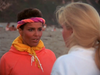 Two women talk on a beach, evoking a scene straight from *Kate’s Secret (1986) DVD*. One wears a pink headband and an orange hoodie with a yellow hood, while the other, seen from behind, has long blonde hair and a white top.