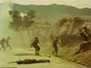 Soldiers in helmets and uniforms advance through a dusty, rugged landscape while smoke rises in the background. In this gripping scene from the Fireball Forward DVD (1972), one figure lies motionless in the foreground as others move towards a rocky hill. Trees and mountains are visible, adding to the suspense and drama that unfolds with every step.