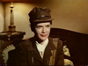 A woman in a military uniform and cap sits on a chair indoors, with a lamp on a table behind her, looking slightly to the side and smiling softly—evoking the quiet intensity found in classic war dramas like “Fireball Forward” (1972), now available on DVD.