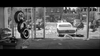 A black and white image shows a city street seen through the glass wall of a tire shop, with stacked tires to the left and a classic car parked outside—evoking the era captured in The World, The Flesh and the Devil DVD (1959)—while litter is scattered across the ground.
