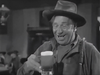 A smiling man in casual attire and a hat holds a foamy mug of beer in a lively, old-fashioned bar scene evoking the classic Western atmosphere of “20 Mule Team (1940),” now available on DVD.