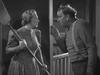 A woman holding a large wooden paddle confronts a man, who gestures and leans toward her, in a dimly lit room. Both appear tense and locked in a heated argument, evoking the dramatic intensity of a classic Western or borax mining film like 20 Mule Team (1940) DVD.