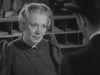 A woman with light hair and a brooch at her collar gazes at a man in a dark suit and hat in a black-and-white setting, possibly from an old classic Western film, with shelves visible behind them—a striking scene reminiscent of vintage movies available on DVD, such as the 20 Mule Team (1940) DVD.