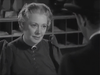 An older woman with light hair in an updo, dressed in a dark gown adorned with a brooch at the collar, is seated facing a man in a hat within a black-and-white office or reception area—perfectly evoking the classic Western ambiance showcased in “20 Mule Team (1940) DVD.”.