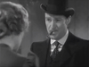 A man in a suit and bowler hat holds a cigar in his mouth, gazing at a woman whose back is to the camera in a black-and-white scene—evoking the timeless atmosphere of classic films like “20 Mule Team (1940)” now available on DVD for devoted collectors.