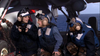 Three people in navy uniforms and helmets sit inside a military aircraft, with the ocean visible beyond. Two are smiling and conversing while the third looks on, all outfitted in protective gear and communication headsets—a heartwarming moment reminiscent of a military family movie such as “Tiger Cruise (2004) DVD.”.