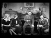 Four adults in formal attire sit in a vintage living room, with a decorated piano and ornate furniture in the background—a scene evoking the elegant settings of classic films like *Make Way For Tomorrow* (1937) on DVD. Three are seated on a couch, one on a chair, all appearing engaged in conversation reminiscent of unforgettable moments from rare DVDs treasured by collectors.