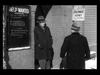 Two men in coats and hats talk outside a brick employment agency, beneath a HELP WANTED sign and a board with handwritten text displayed on the wall. Snow is falling as one man leans against the building—a classic scene reminiscent of hard-to-find films like Make Way For Tomorrow DVD (1937).