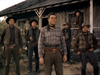 A group of men in cowboy attire stand outside a wooden building, some holding guns, conjuring the gritty excitement of cowboy cinema. The scene is reminiscent of a classic Western film such as Gun Belt (1953), evoking timeless moments beloved by collectors of classic western DVDs and rare movies on DVD alike.