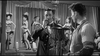 A man in a suit smokes a cigar as can-can dancers perform on stage in this black-and-white scene from Man With The Gun (1955) DVD—perfect for fans of rare movies.