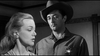A woman in profile speaks as a stern man in a sheriff’s uniform and cowboy hat listens in this black-and-white scene from Man With The Gun (1955) DVD.